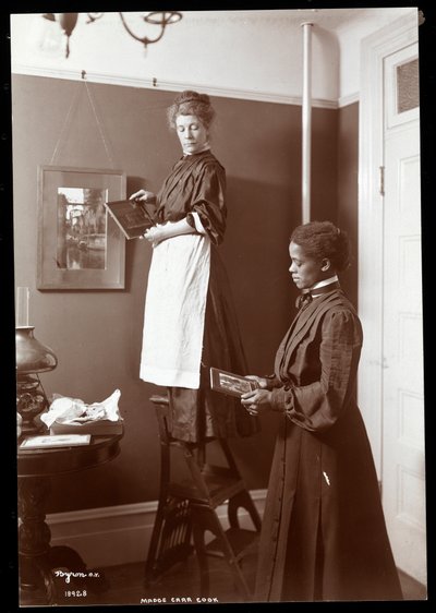 Madge Carr Cook hanging pictures with her maid by Byron Company